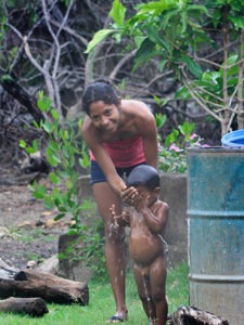 Girl gives her little brother a bath with a bucket in Playa Gigante, Nicaragua.